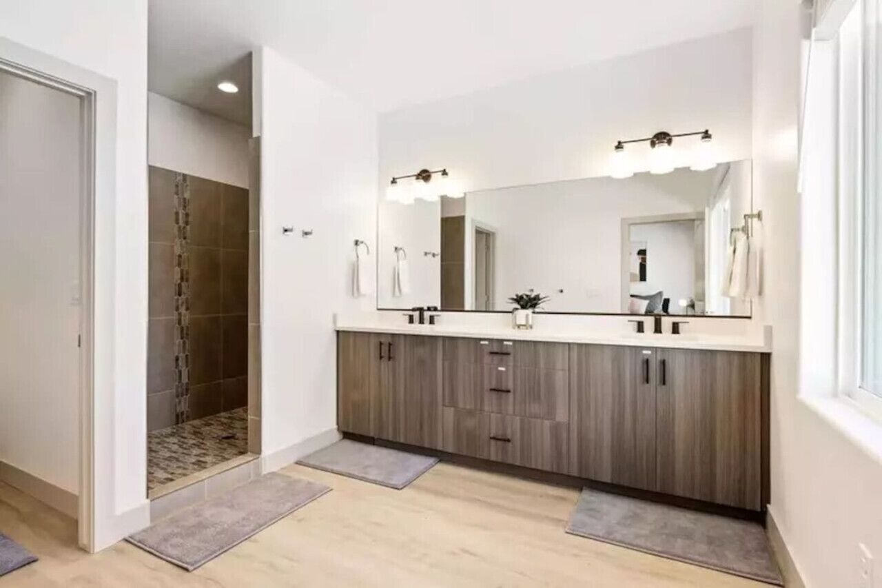 Un baño moderno con un espejo grande, lavamanos dobles y zona de ducha.