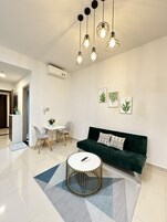 Un salón moderno con un sofá verde, una mesa de centro redonda y un comedor con una mesa blanca y dos sillas.
