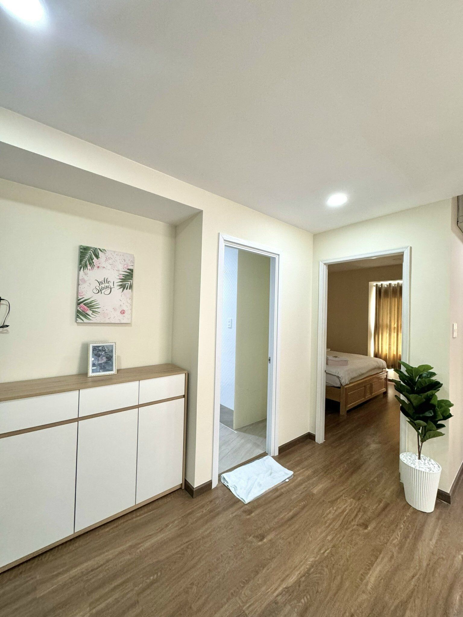A hallway leading to a bedroom with a bed, a bedside table, and a potted plant.