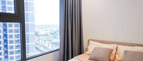 A hotel room with a large window, a bed with beige bedding, and a view of a cityscape.