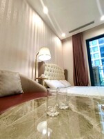 Quarto de hotel com cama, sofá, abajur e mesa de vidro.