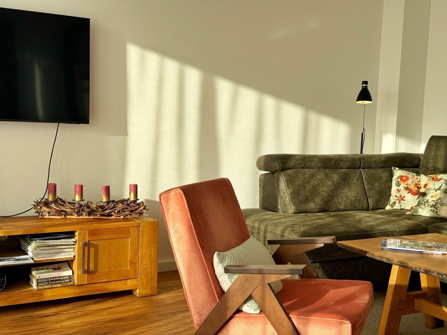 Ein modernes Wohnzimmer mit einem Holzschrank, einem roten Sessel, einem grünen Sofa und einem kleinen Tisch.
