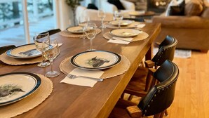 Una taula de dinar preparada amb plats, gots i coberts, amb una llar de foc i un sofà al fons.