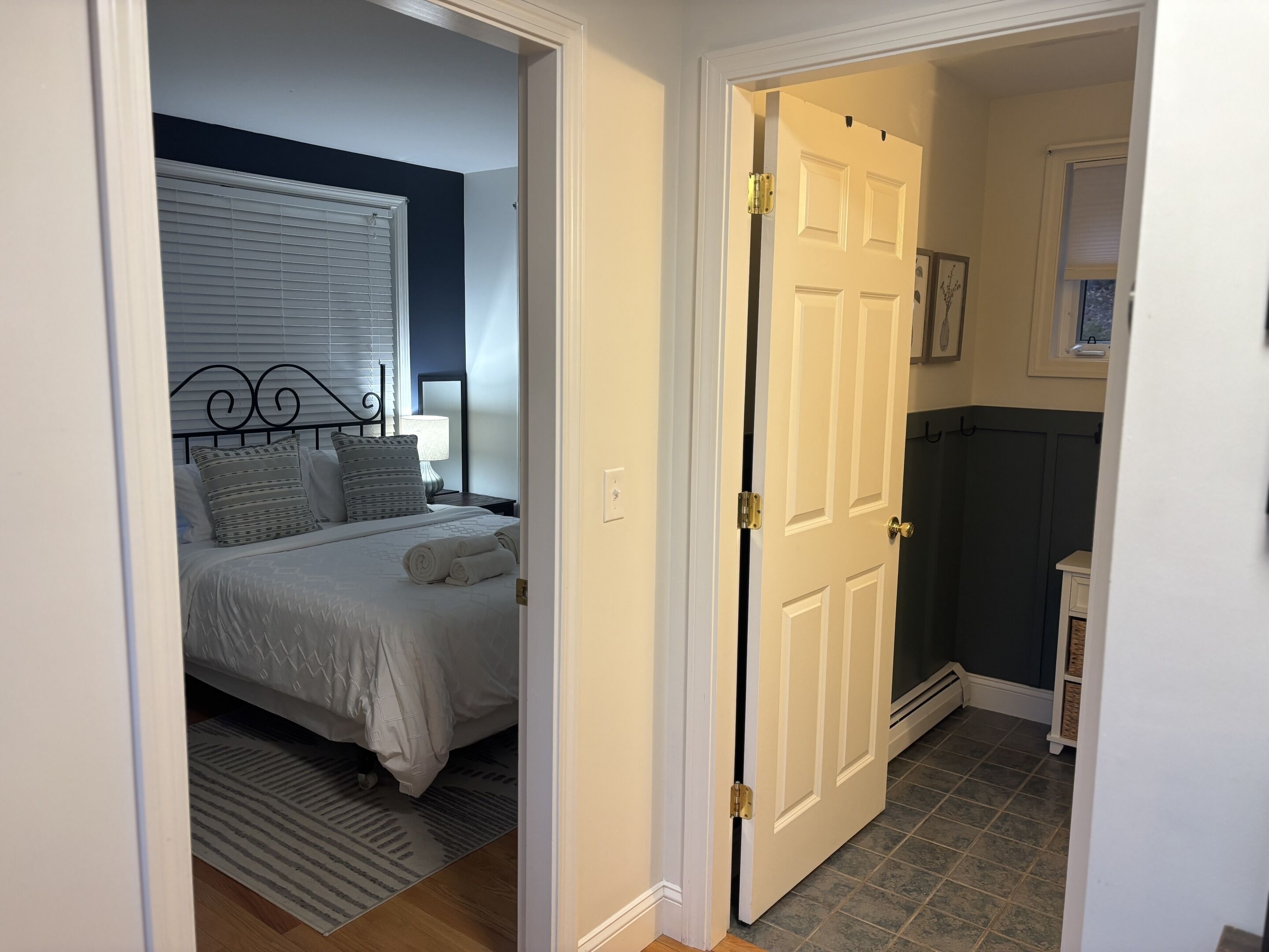 A bedroom with a bed, bedside table, lamp, and a door leading to another room.