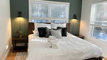 A bedroom with a bed, two bedside tables, a nightstand, a window with blinds, and a lamp on each side.