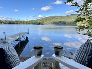 Une vue sur le lac, avec deux tasses posées sur une chaise blanche, une jetée et une colline boisée en arrière-plan.