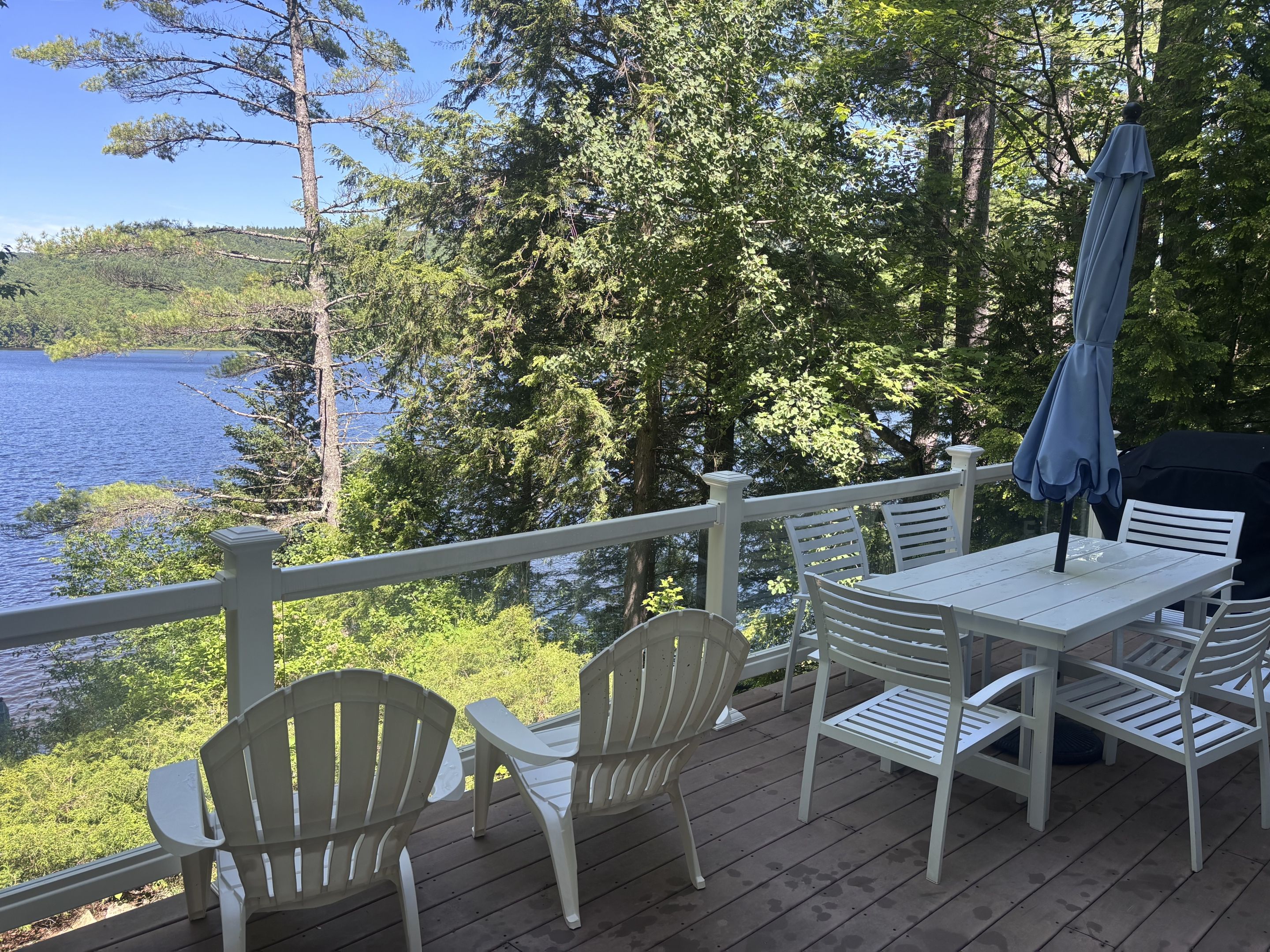 Una terraza con mesa y sillas que da a un lago, rodeada de árboles.