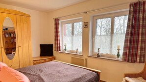 Une chambre à coucher avec un lit, une armoire en bois, une télévision et une fenêtre avec des rideaux.