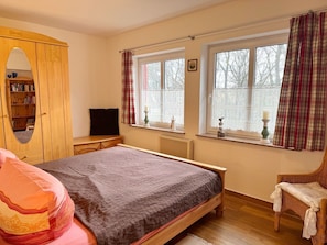 Een slaapkamer met een bed, een houten garderobe, een televisie en een raam met gordijnen.