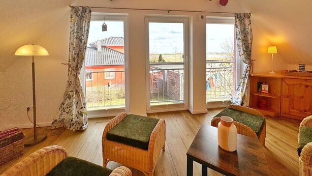 Une pièce chaleureuse avec un plafond en bois, une table à manger avec des chaises, un lampadaire et une vue sur une maison à travers de grandes fenêtres.