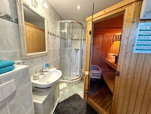 Een badkamer met een douche, wastafel en een houten sauna.