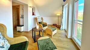 Une pièce confortable de style loft, avec de hauts plafonds, des poutres en bois, une grande fenêtre, des meubles en osier et une petite table.