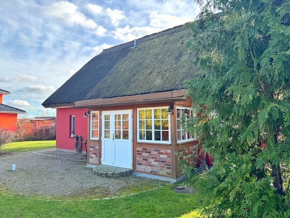 A small, single-story house with a thatched roof, a red brick exterior, and a white door.