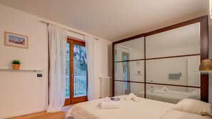 Ein Schlafzimmer mit einem großen Bett, einem Fenster mit Vorhängen, einem Heizkörper und einer kleinen Pflanze auf einem Regal.