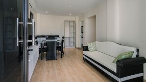 A modern living room with a sofa, a dining area with chairs, a kitchen in the background, and a glass door leading outside. - Sonrisa Resort de Playa by Hiverooms (San Remigio)