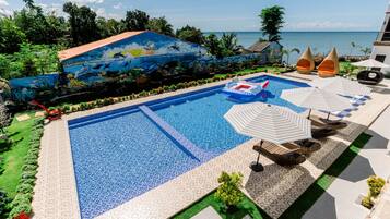 Una piscina con un mural, sillas de descanso, sombrillas y vistas al océano.