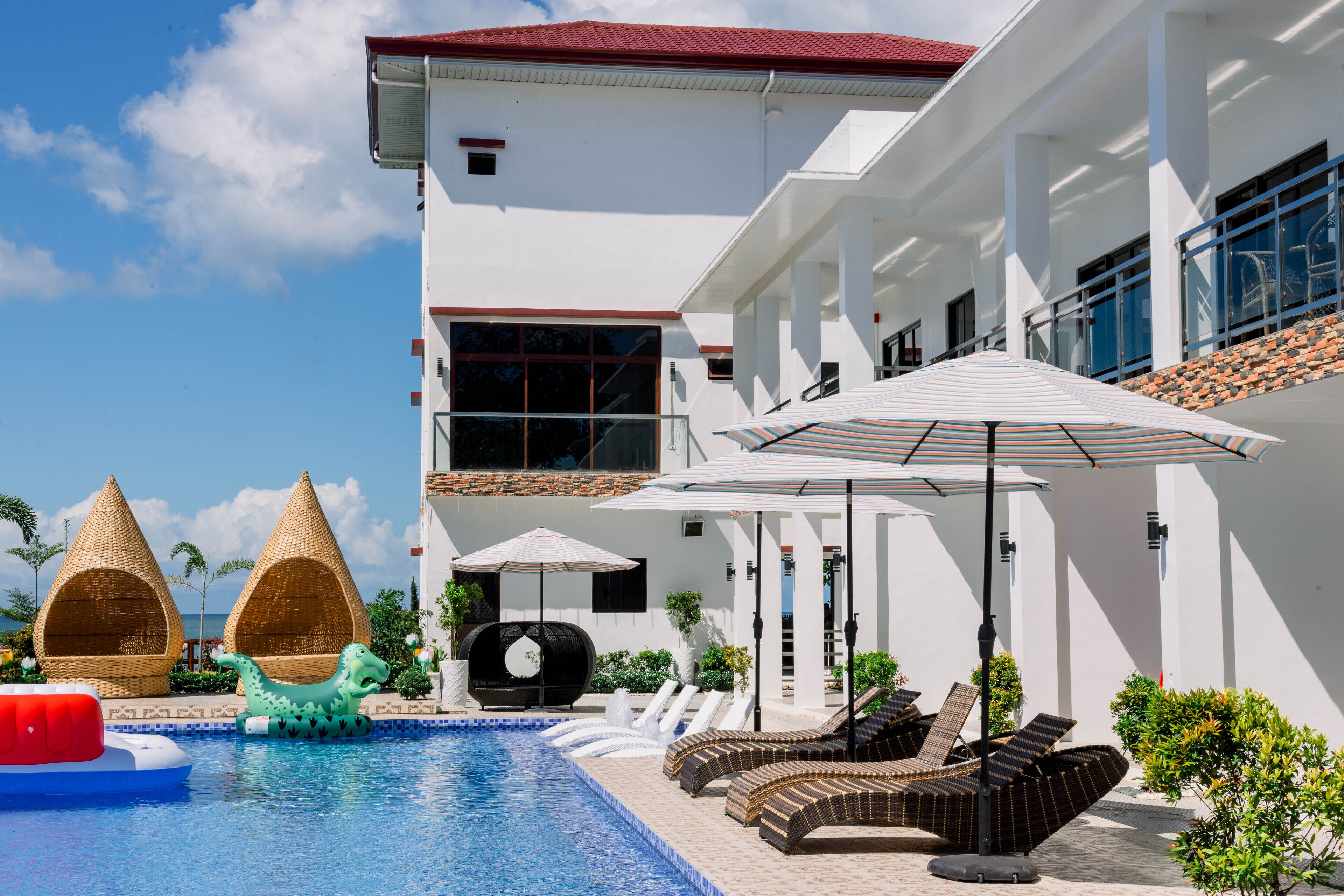 A pool area with lounge chairs, a water slide, and a building with a red roof.