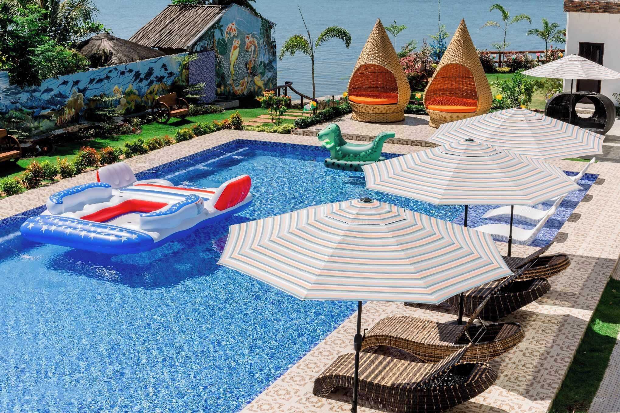 A swimming pool with lounge chairs and umbrellas, surrounded by a landscaped garden and a mural.
