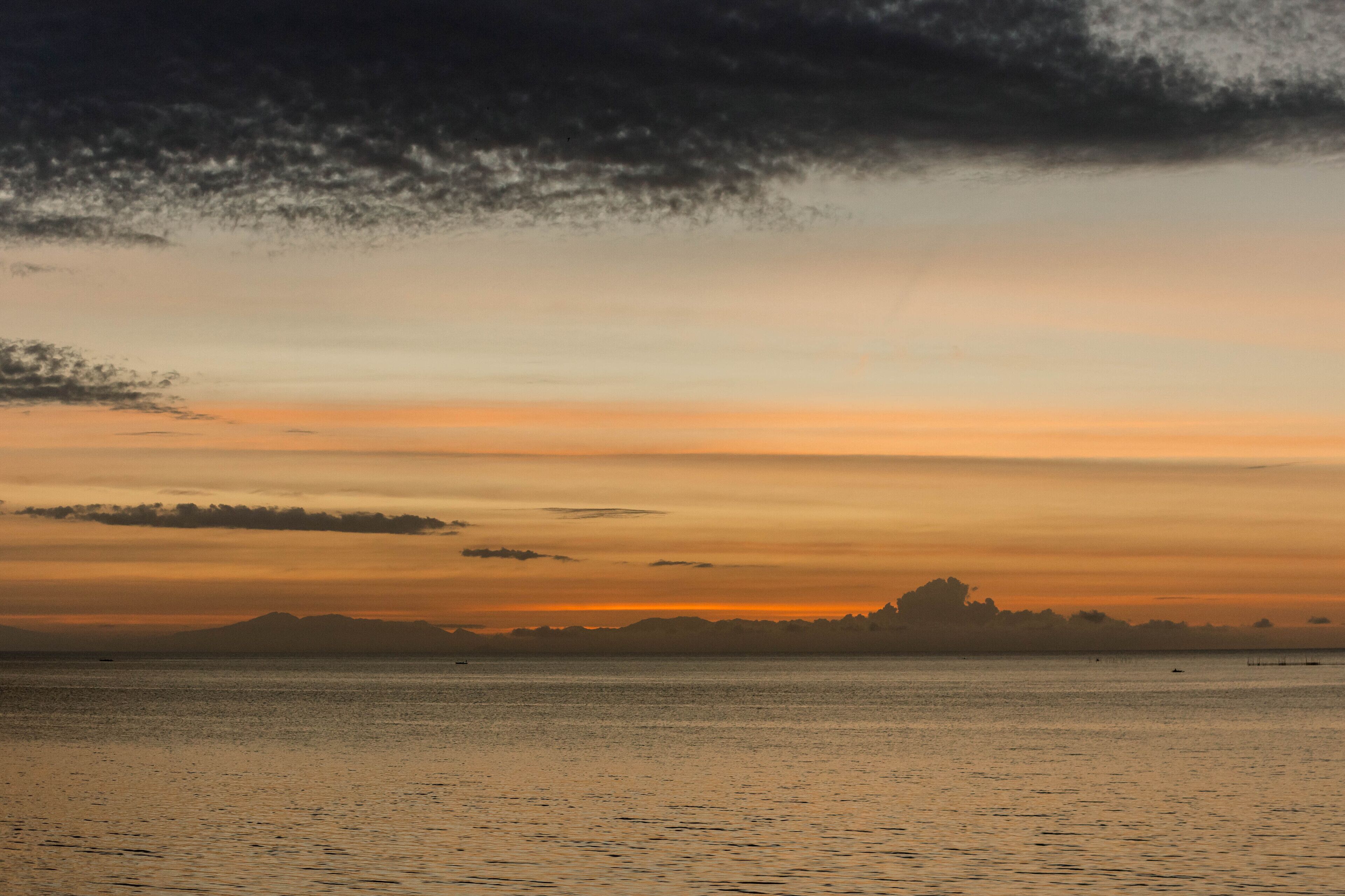 Un atardecer sobre un mar tranquilo con siluetas de tierra en la distancia.
