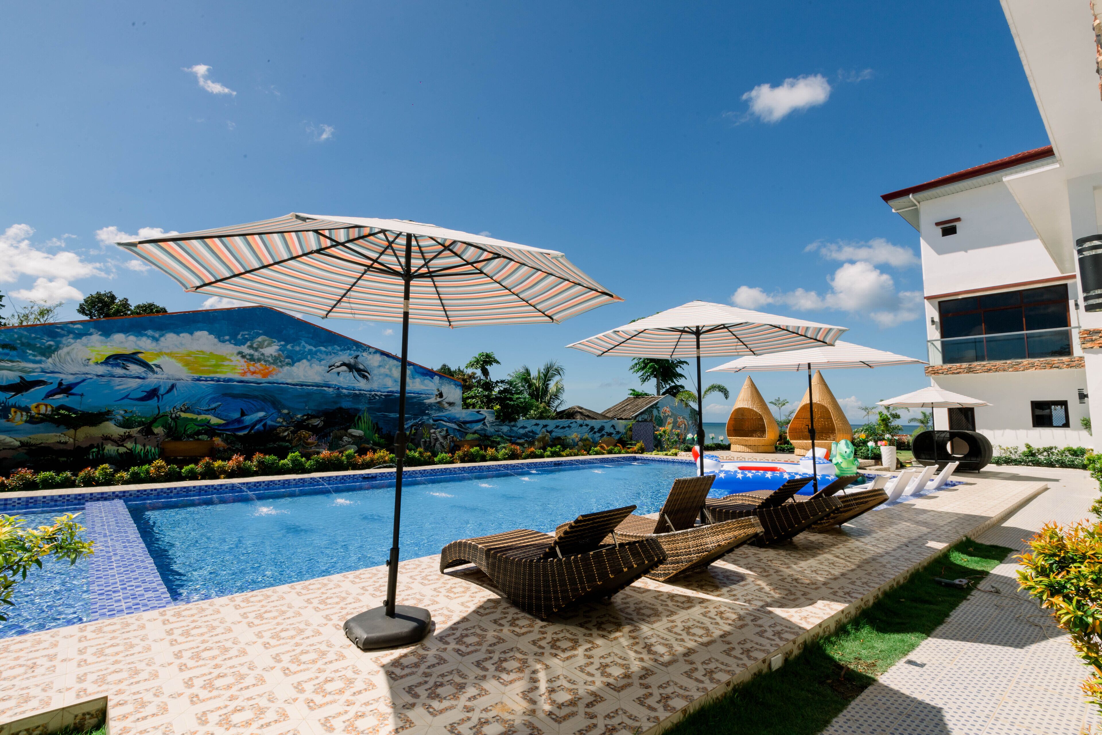 A pool area with lounge chairs and umbrellas, a mural, and a building with a white facade.