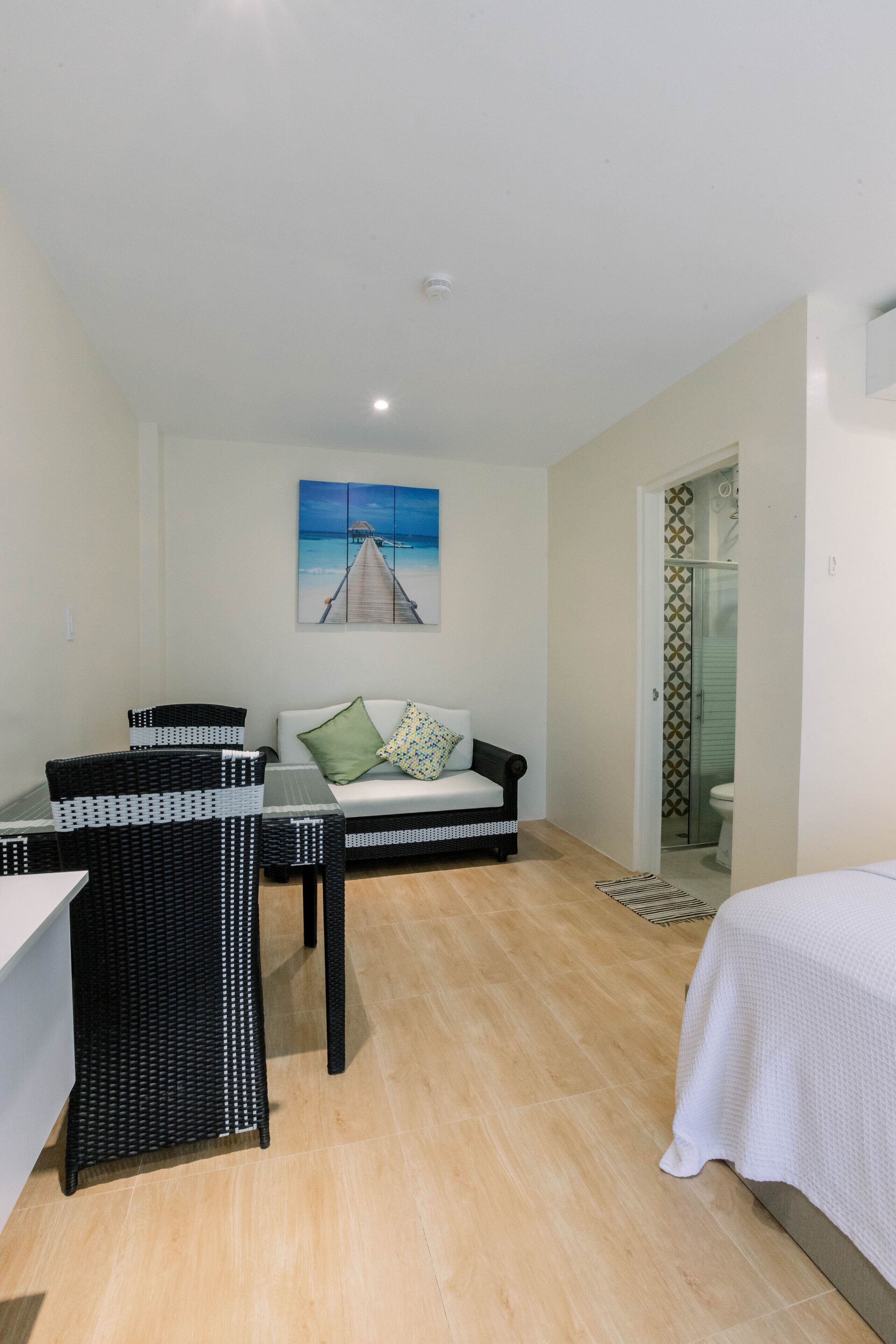 A room with a bed, a sofa, a dining table, and a painting of a pier.