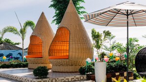 A building with a unique conical design, surrounded by a garden with palm trees and a large striped umbrella. - Sonrisa Resort de Playa by Hiverooms (San Remigio)