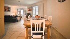A dining area with a wooden table and chairs, a large wall clock, and a view into the living room. - La Parie 1 by Interhome (Ile d'Oléron)