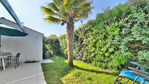 A patio area with a table and chairs, a palm tree, and a blue kayak. - La Parie 1 by Interhome (Ile d'Oléron)