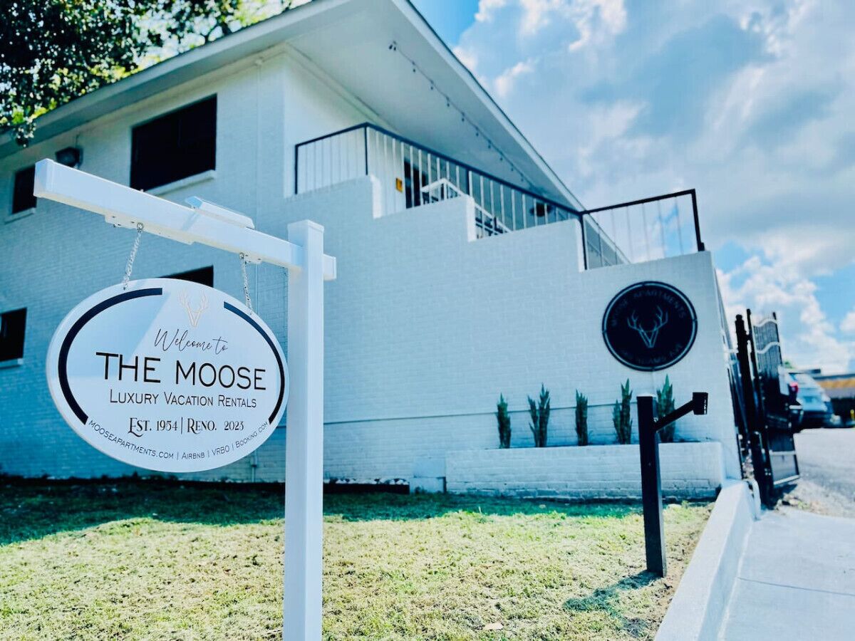 A sign for 'The Moose Luxury Vacation Rentals' with a modern building in the background.
