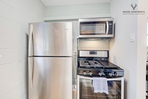 A compact kitchen with a stainless steel refrigerator, a microwave, and a gas stove.