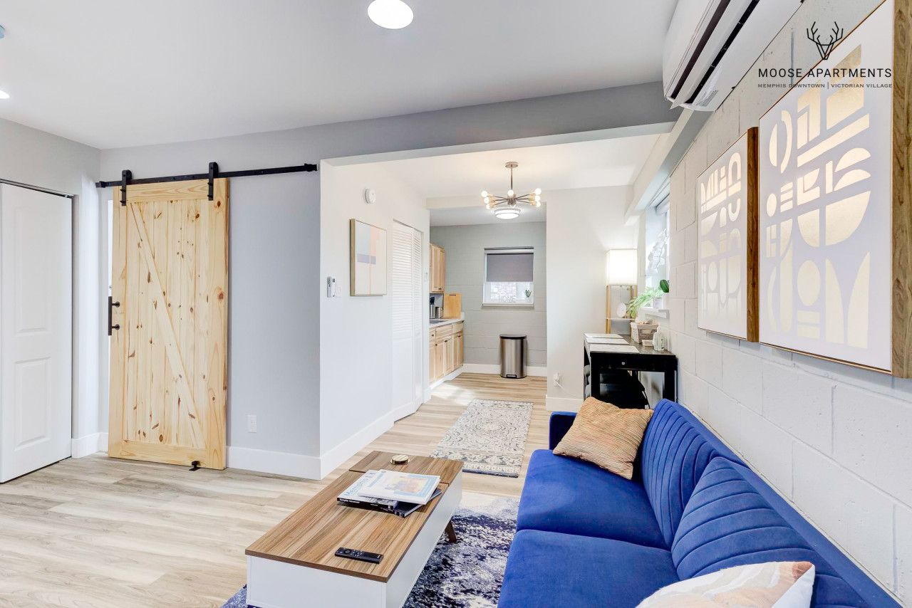 A modern apartment interior with a blue sofa, wooden coffee table, and a sliding barn door.