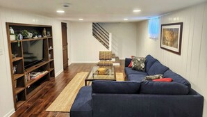 A living room with a dark blue sofa, a glass coffee table, a wooden bookshelf, and a staircase leading to another level.