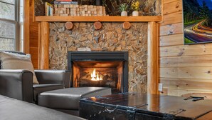 A cozy living room with a stone fireplace, leather furniture, and a wooden wall. - Epic Views • One Level • Hot Tub • Huge Fenced Yard • Pet Friendly • Easy Roads (Sevierville)