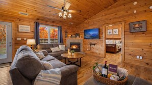 A cozy cabin interior with a sofa, a fireplace, a television, and a welcome sign. - Epic Views • One Level • Hot Tub • Huge Fenced Yard • Pet Friendly • Easy Roads (Sevierville)
