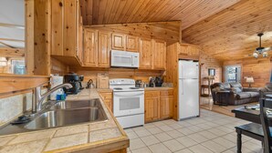 A kitchen with wooden cabinets, a stove, a microwave, and a refrigerator. - Epic Views • One Level • Hot Tub • Huge Fenced Yard • Pet Friendly • Easy Roads (Sevierville)