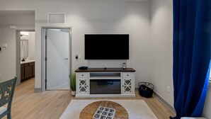 Una sala de estar moderna con un televisor de pantalla plana montado en un mueble blanco, una puerta que da a una cocina y una cortina azul a la derecha.