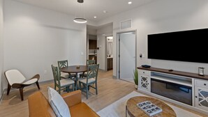 Una sala moderna con un televisor de pantalla plana, un comedor con sillas y una mesa, y una cocina al fondo.