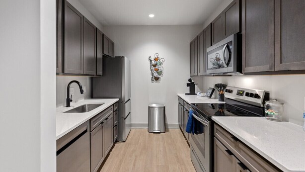 Una cocina moderna con electrodomésticos de acero inoxidable, encimeras blancas y armarios de madera oscura.