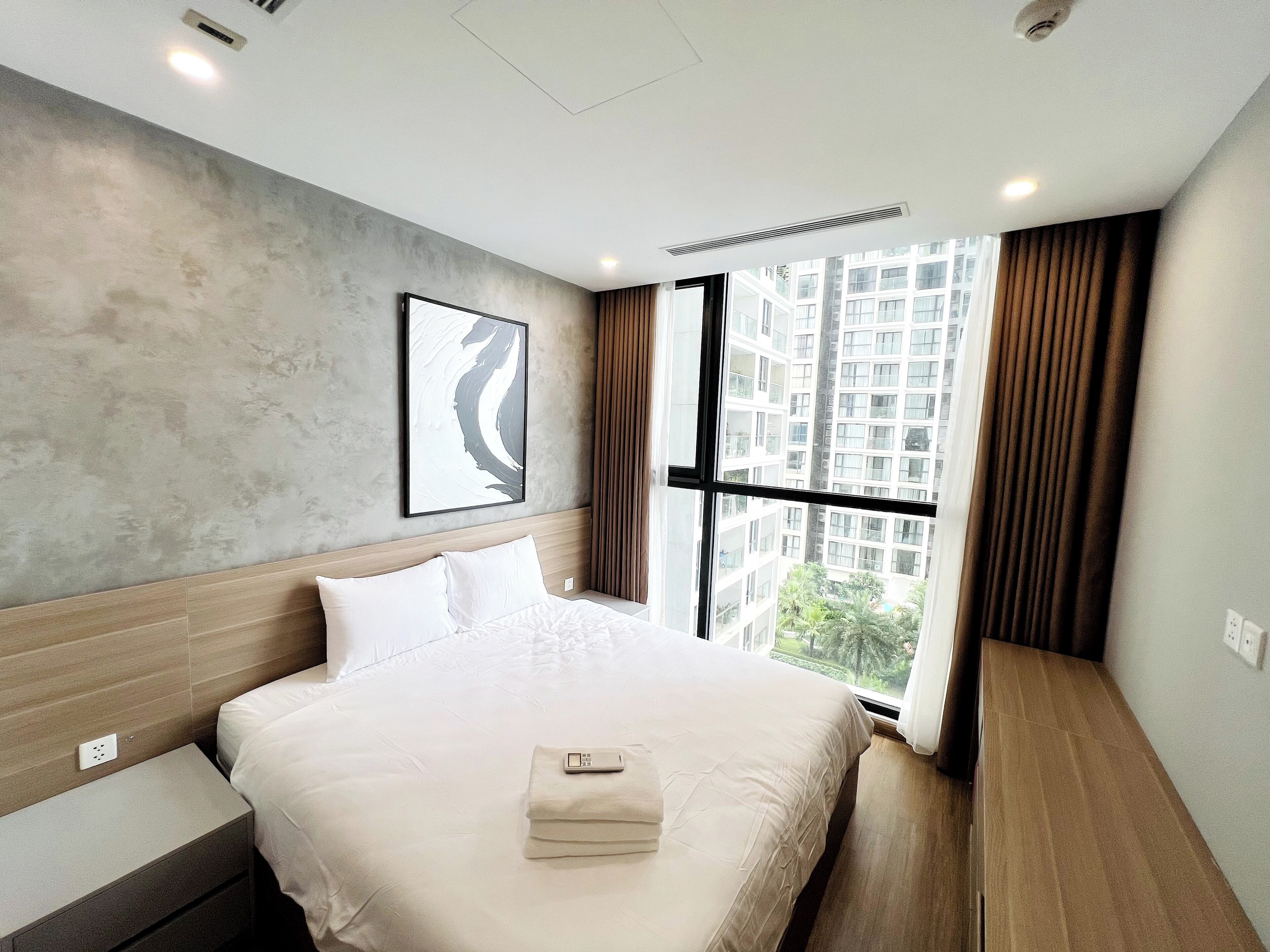 A modern hotel room with a large bed, a view of a cityscape, and a window with curtains.