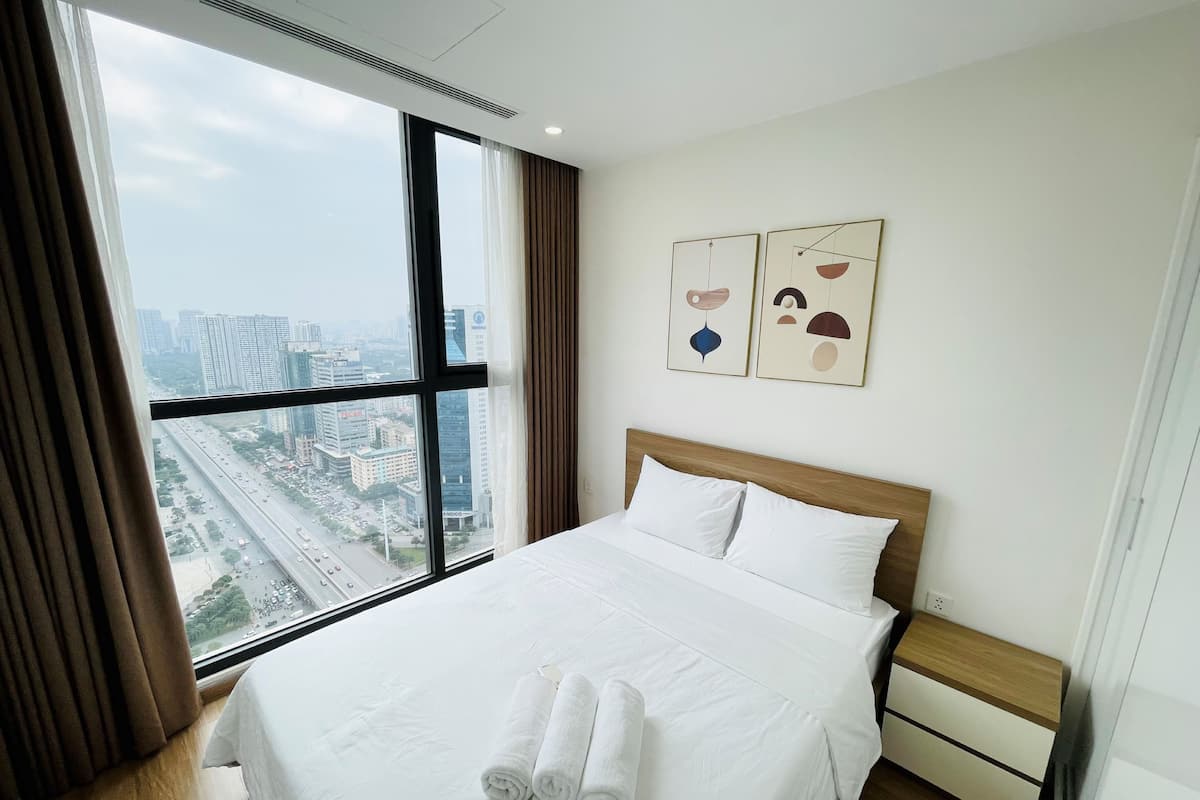 Ein Hotelzimmer mit großem Fenster, einem Bett mit weißen Leinentüchern, einem Holz-Kopfteil und zwei an der Wand befestigten Kunstwerken.