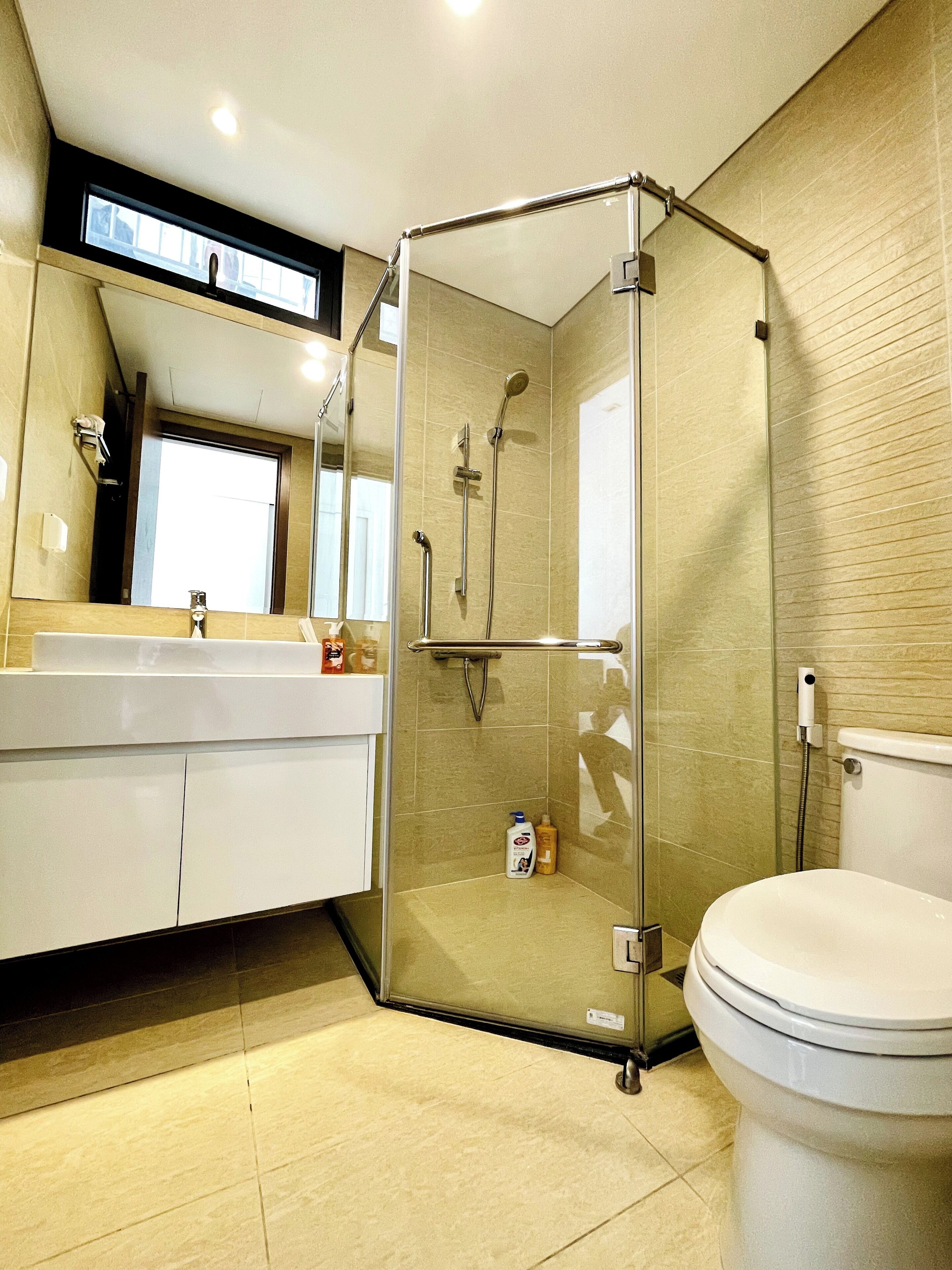 Ein modernes Badezimmer mit einer gläsernen Dusche, einer weißen Toilette und einem Waschbecken mit Pflegeprodukten.