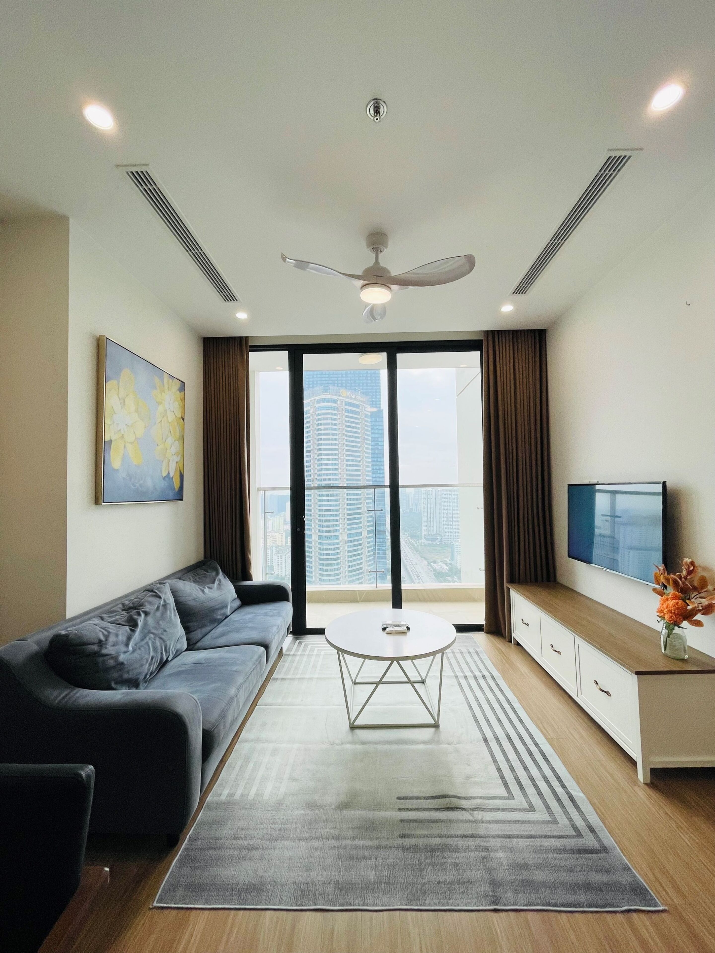 A modern living room with a grey sofa, a round coffee table, and a TV on a wooden cabinet.