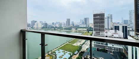 A cityscape view from a balcony with a river and park in the foreground, modern buildings in the background.