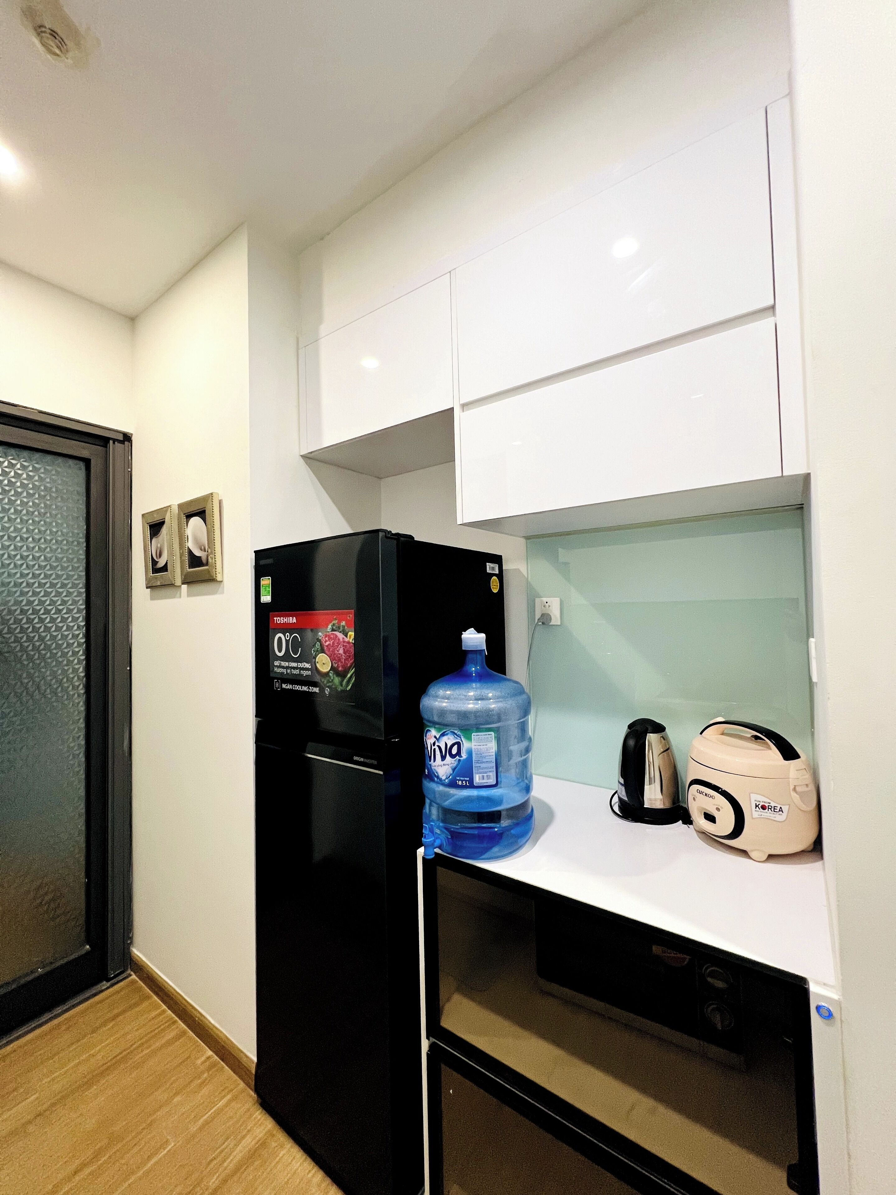 A compact kitchenette with a black refrigerator, a large water dispenser, a toaster, and a kettle.