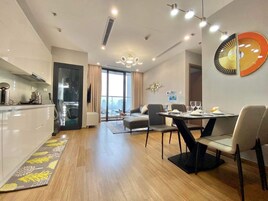 Un apartamento moderno con cocina, comedor y sala de estar. Cuenta con un amplio ventanal con vista a la ciudad, una araña y un dispensador de agua.