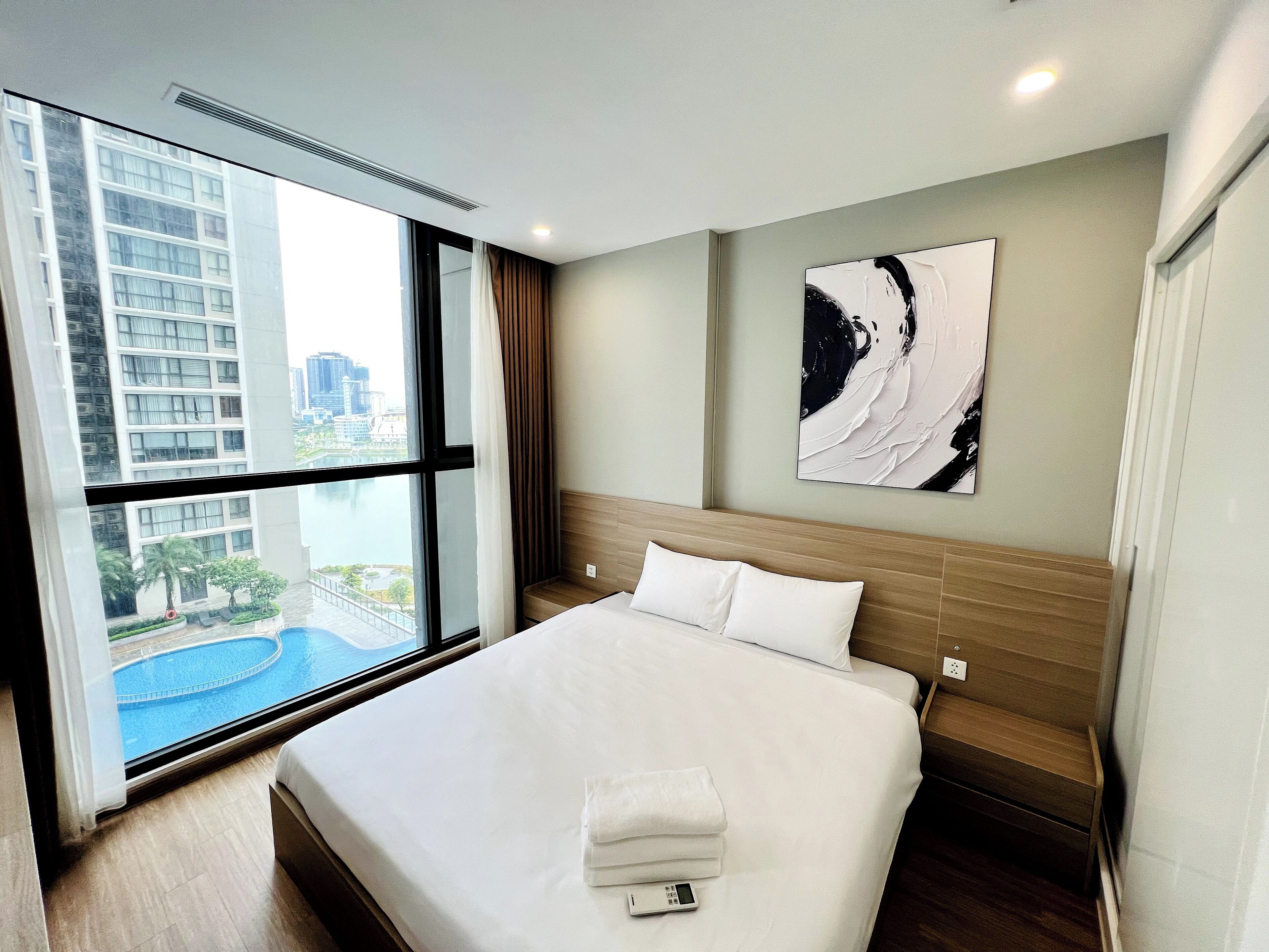 Ein Hotelzimmer mit einem großen Bett, Blick auf einen Pool und eine Stadtlandschaft durch das Fenster.