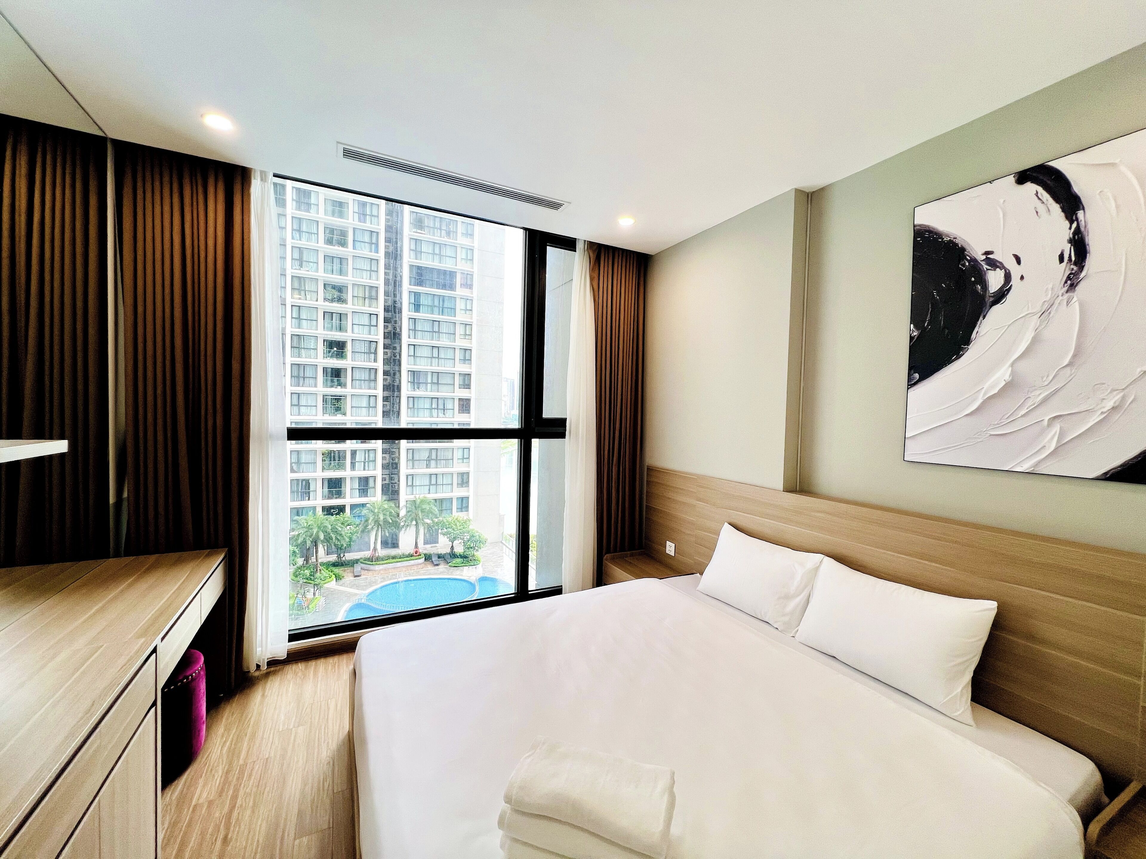 Habitación de hotel con una cama grande, un escritorio y un ventanal con vistas a un edificio y una piscina.