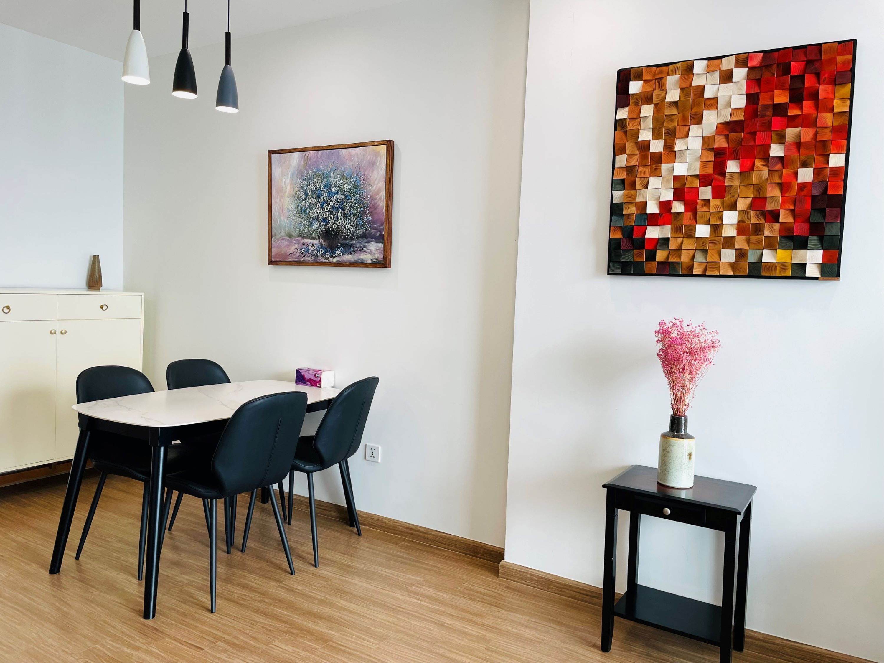 A dining area with a table and chairs, a painting, and a decorative wall piece.