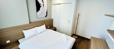 Quarto de hotel com uma cama grande, cabeceira de madeira, um cabideiro e uma pintura abstrata pendurada na parede.