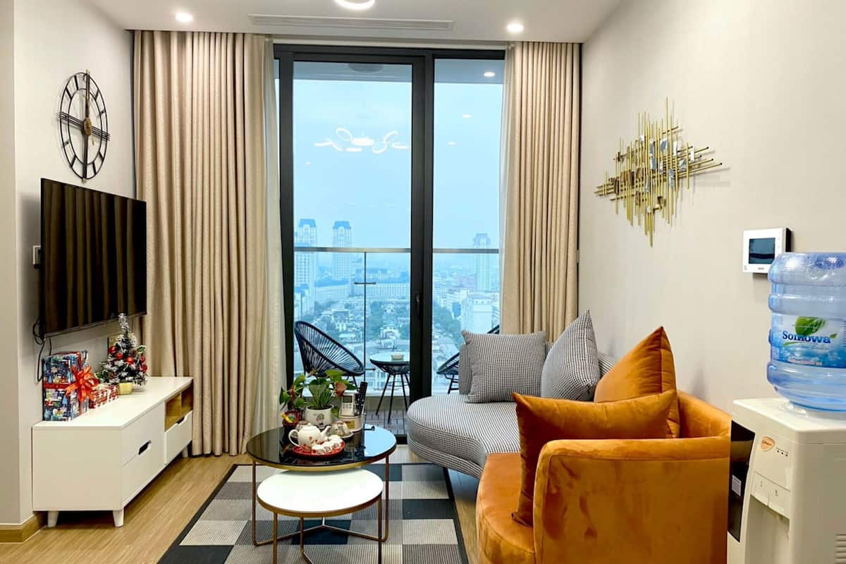 Ein modernes Wohnzimmer mit großem Fenster, einem Flachbildfernseher, einem Wasserspender und einer gemütlichen Sitzecke mit Sofa und Sesseln.